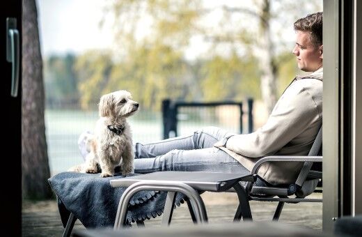 Mann mit Hund auf Liegestuhl im Ferienhaus